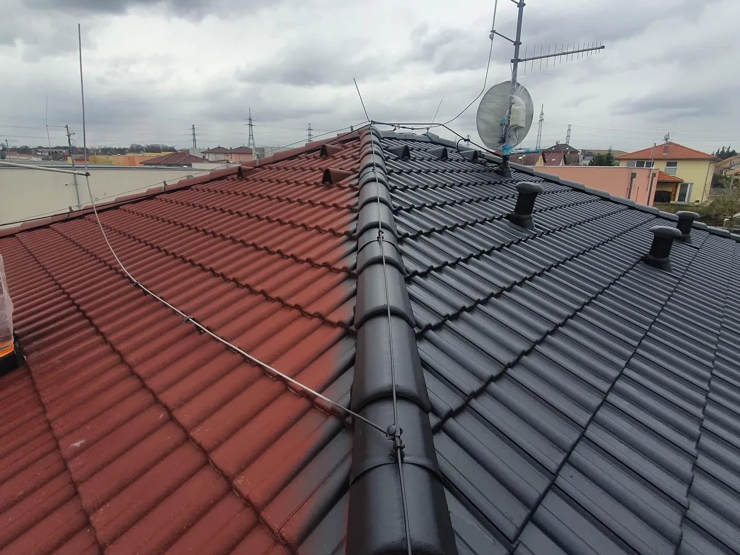 Betonová tašková střecha rodinného domu v průběhu renovace: pravá polovina po dvojitém horkém nástřiku v antracitu, levá polovina v původní červené