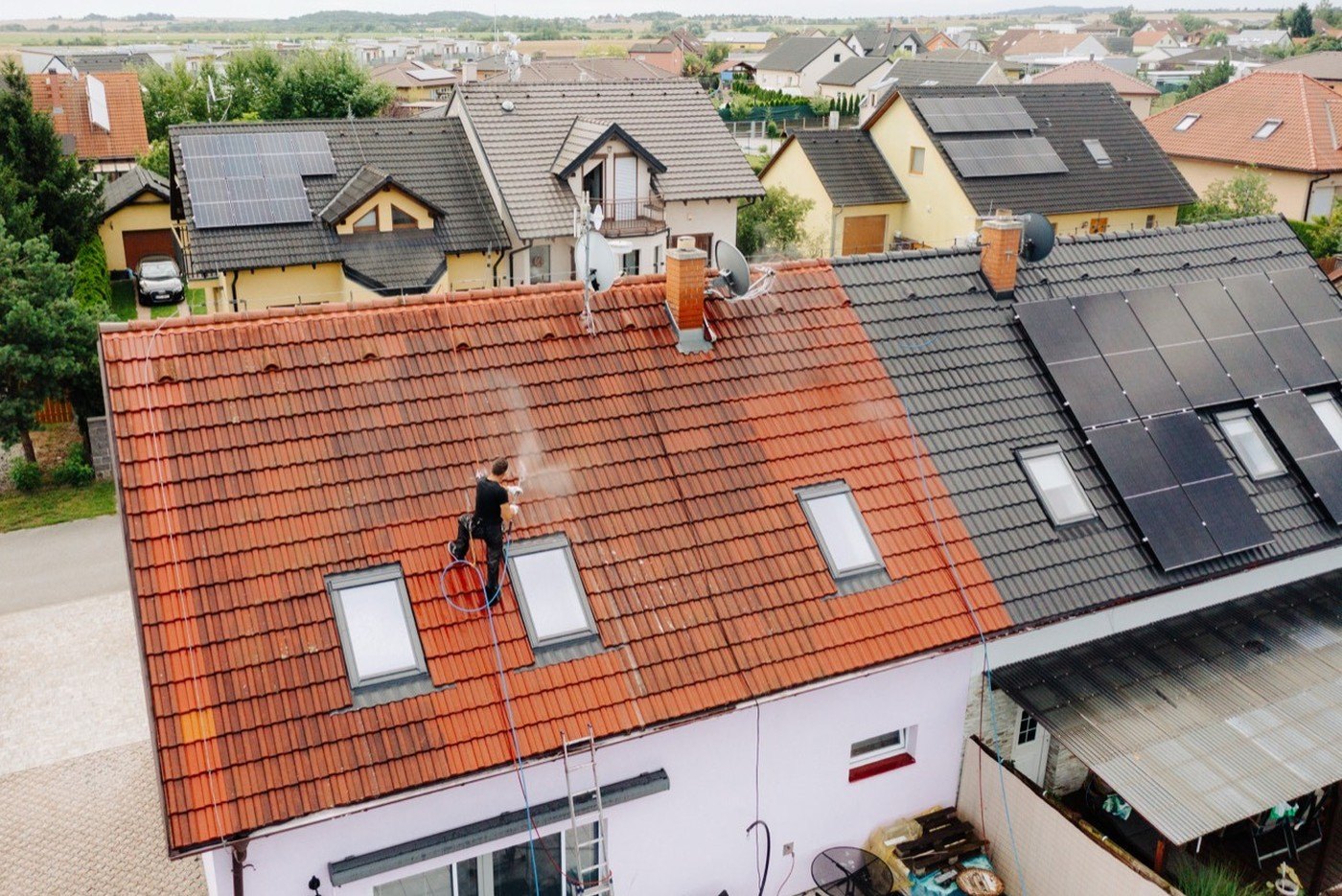 Technik čistí taškovou střechu tlakovou vodou z lana, vedle jsou fotovoltaické panely