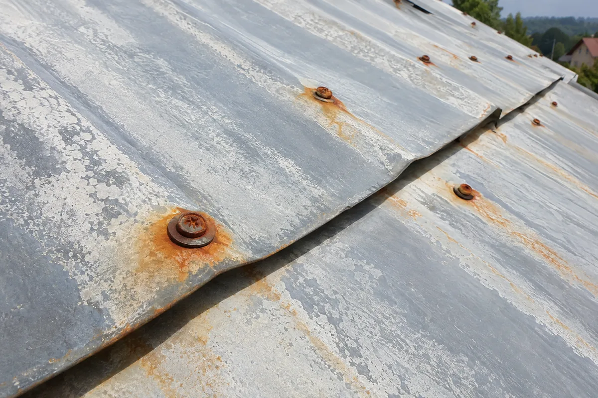 Rez u šroubů a vybledlý povrch staré plechové střechy před renovací